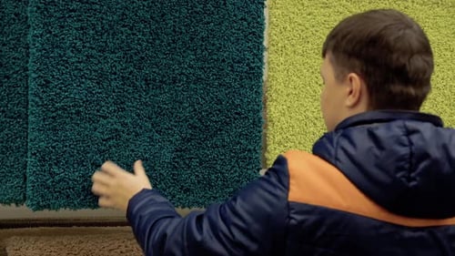 Young Guy Chooses Carpet in the Building Materials Store with the Purpose of Buying
