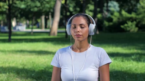 Girl Doing Yoga in the Park and Listening Music on Headphones. Sunny Day