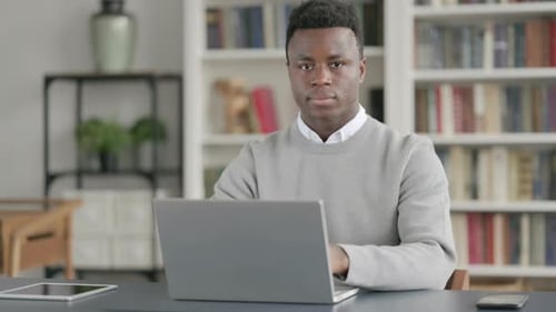 African Man Smiling at Camera While Using Laptop in Library