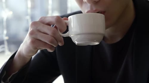 Nahaufnahme eines ernsthaften gutaussehenden Mannes, der in einem Café einen Schluck von einer Tasse Tee nimmt