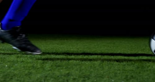Soccer Player Kicking Ball on Field at Night