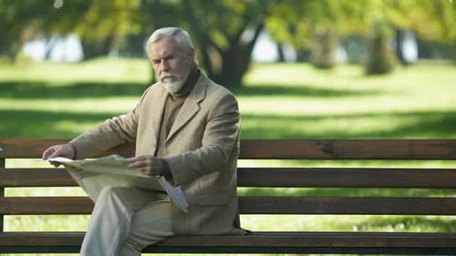 Senior Man Reading Newspaper on Park Bench