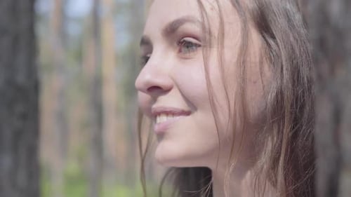 Nahaufnahme Porträt einer glücklich lächelnden jungen Frau, die sich im Kiefernwald umschaut. Konzept des Campings