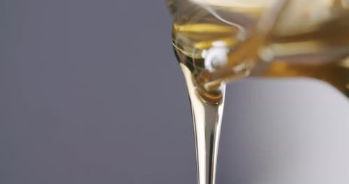 Macro close up shot of viscous honey flowing out of a honey jar before a grey studio background. Sta