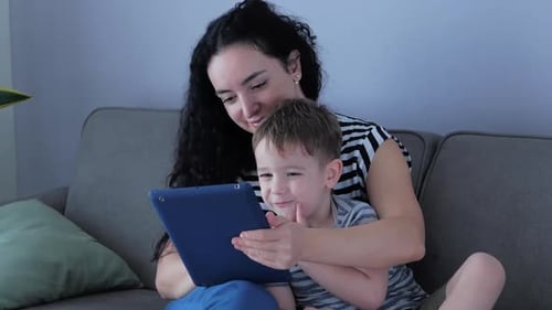 Mother and Son with Tablet Indoors on Gray Couch