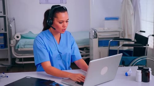 Woman in Scrubs Works at Hospital Desk with Laptop