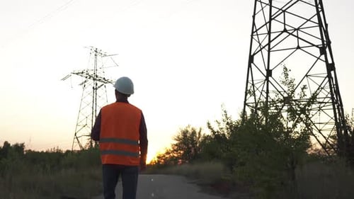 Electrical Engineer Walking Towards Power Line Tower at Sunset