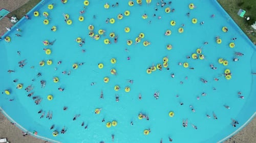 Top view: Lots of people swim and have fun in the big pool under the open air on a sunny, hot day.