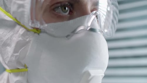 Hospital Worker in Protective Respirator Mask, Suit and Glasses Looking Away