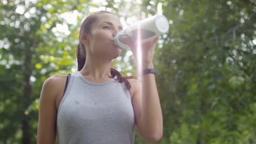 Beautiful Sportswoman Drinking Water and Smiling at Camera in Park