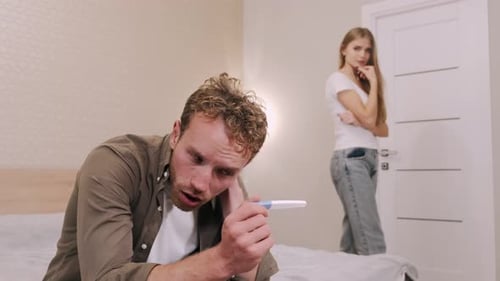 Frustrierter junger Mann schaut sich Schwangerschaftstest zu Hause an