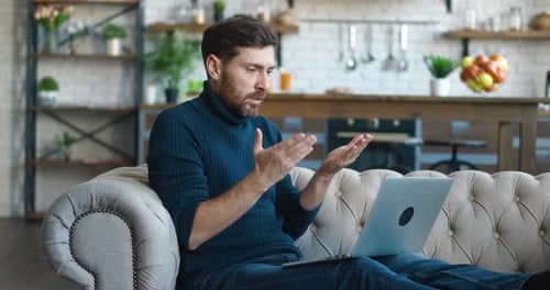 Side View Bearded Man Entrepreneur Talking Video Call at Home Sitting on the Sofa at Home
