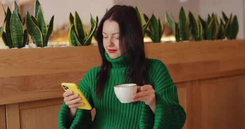Woman Using Phone and Drinking Coffee in Cafe