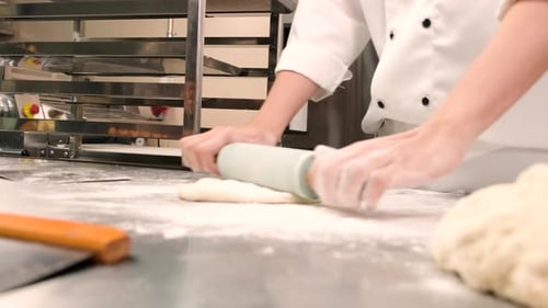Chef is preparing pastry dough, baking bakery food on a stainless steel table.