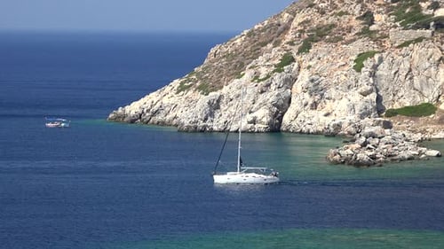 Un voilier blanc longe la côte rocheuse dans la mer