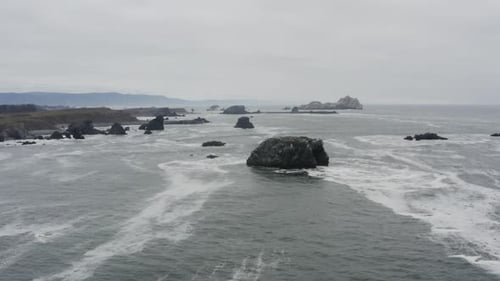 Stürmische Tagesantenne einer felsigen Küste, die auf einen großen Felsen im Meer zusteuert, Wellen stürzen aga