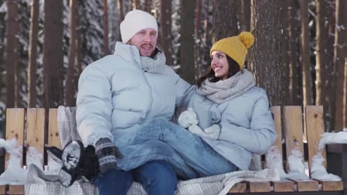 Young Couple Relax in a Winter Forest and Communicate a Man and a Young Woman Sit on a Swing and