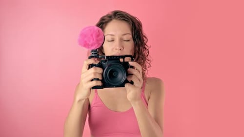 Woman Smiling Holding Camera with Microphone on Pink