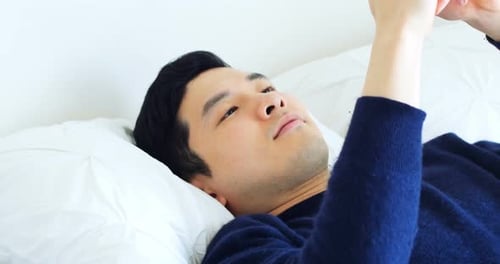 Man Relaxing in Bed Using Mobile Phone