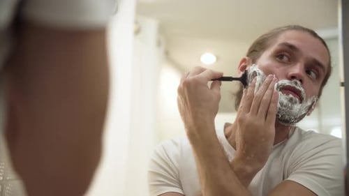 Homem raspando barba com navalha no banheiro