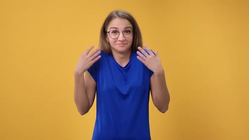 Woman Shrugging, Indicating Uncertainty on Yellow Backdrop