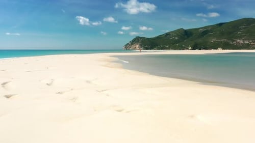 Un hombre caminando por la playa de arena con un magnífico acantilado en el fondo