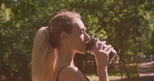 Athletic Woman Drinking from Shaker Bottle in Park