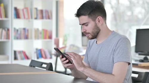 Serious Young Man Using Smartphone in Office