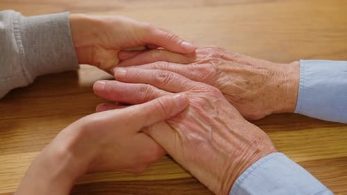 Adult Holds Hands of Senior on Wooden Table