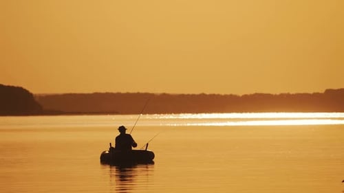 Silhouette eines Mannes mit Hut, der vom Boot aus auf dem abendlichen Flusshintergrund fischt.