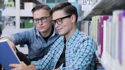 Students Reading Book At College Library Near Bookshelves