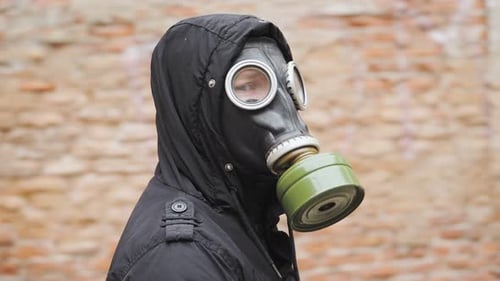 Portrait young man stands in a gas mask and looks around. Doomsday concept.