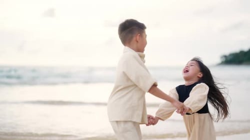 4K Little Asian child boy and girl sibling walking together on the beach at summer sunset.