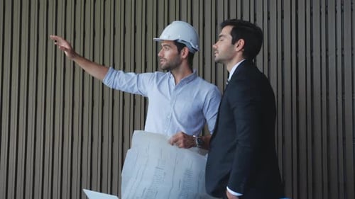 Team engineer planning and examining blueprint and pointing with partner.