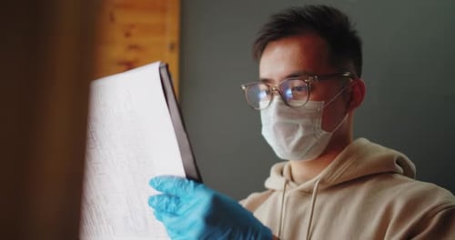 Young Adult in Mask Examines Paperwork