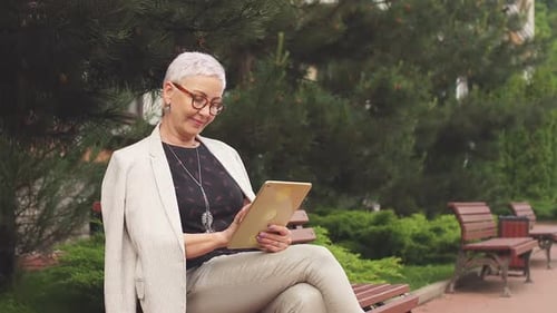 Elegant Cheerful Woman Uses Tablet in Luxury Hotel. Lady Browsing the Net in Park.