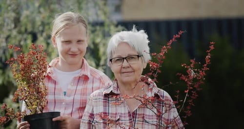 Portrait of an Elderly Woman with Her Granddaughter Holding Potted Plants for Planting in the Garden