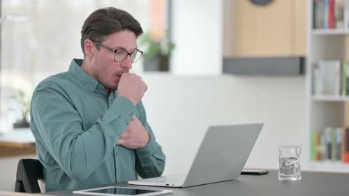 Man Coughing While Working on Laptop at Desk