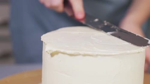 Frau nivelliert eine leichte Creme auf einem Kuchen auf einem rotierenden Ständer in einer Wohnküche