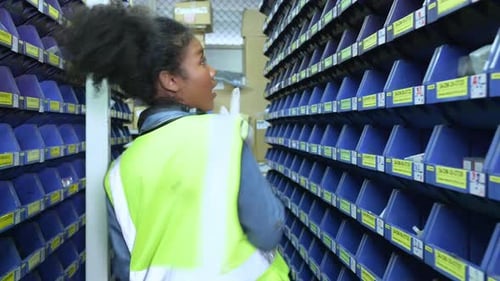 Employé d'entrepôt comptant les petites pièces stockées dans le compartiment de rangement bleu.
