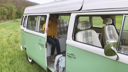 Woman Exits Vintage Camper Van Into Rural Landscape