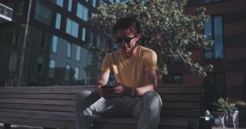 Man smiles while using phone on park bench