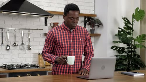 Adult Opens Laptop and Drinks Coffee in Kitchen