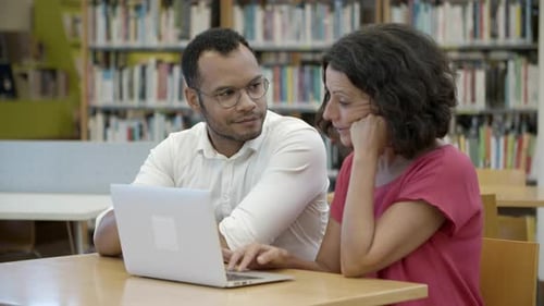 Students Collaborate Using Laptop in Library Setting