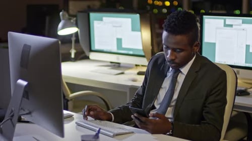 Afrikanischer Büroangestellter arbeitet am Computer und telefoniert