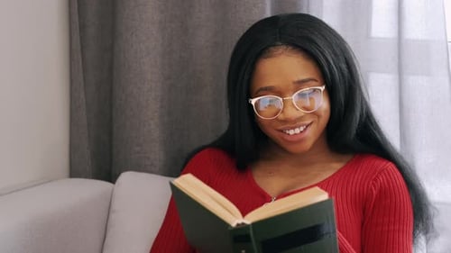 African American Woman Reading a Book Sitting on Bed at Home
