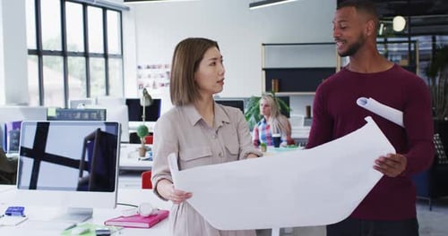 Diverse male and female office colleagues discussing over blueprint plan at modern office