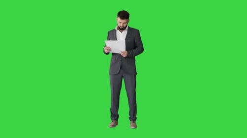 Businessman Standing and Reading Papers Seriously on a Green Screen, Chroma Key.