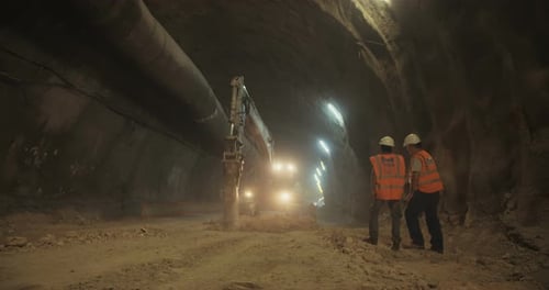 Construction workers supervising heavy machinery during tunnel construction work