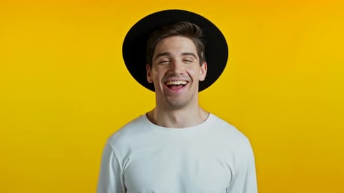 Excited Man with Hat Smiles on Yellow Background
